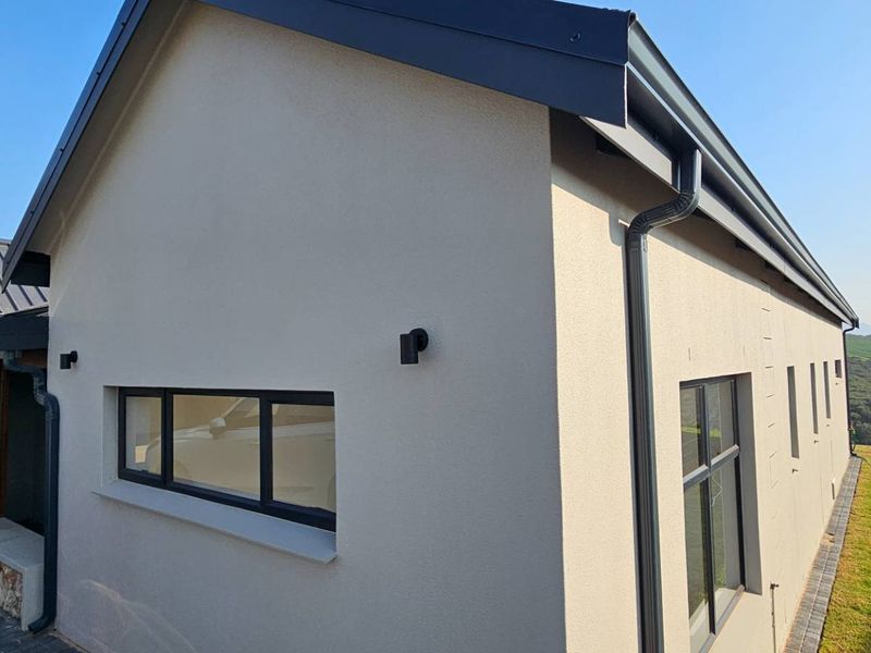A modern exterior view of the property featuring clean rendered walls, dark metal roofing, and contemporary aluminium window frames.