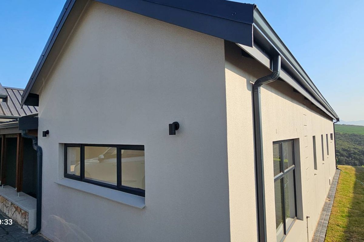 A modern exterior view of the property featuring clean rendered walls, dark metal roofing, and contemporary aluminium window frames.