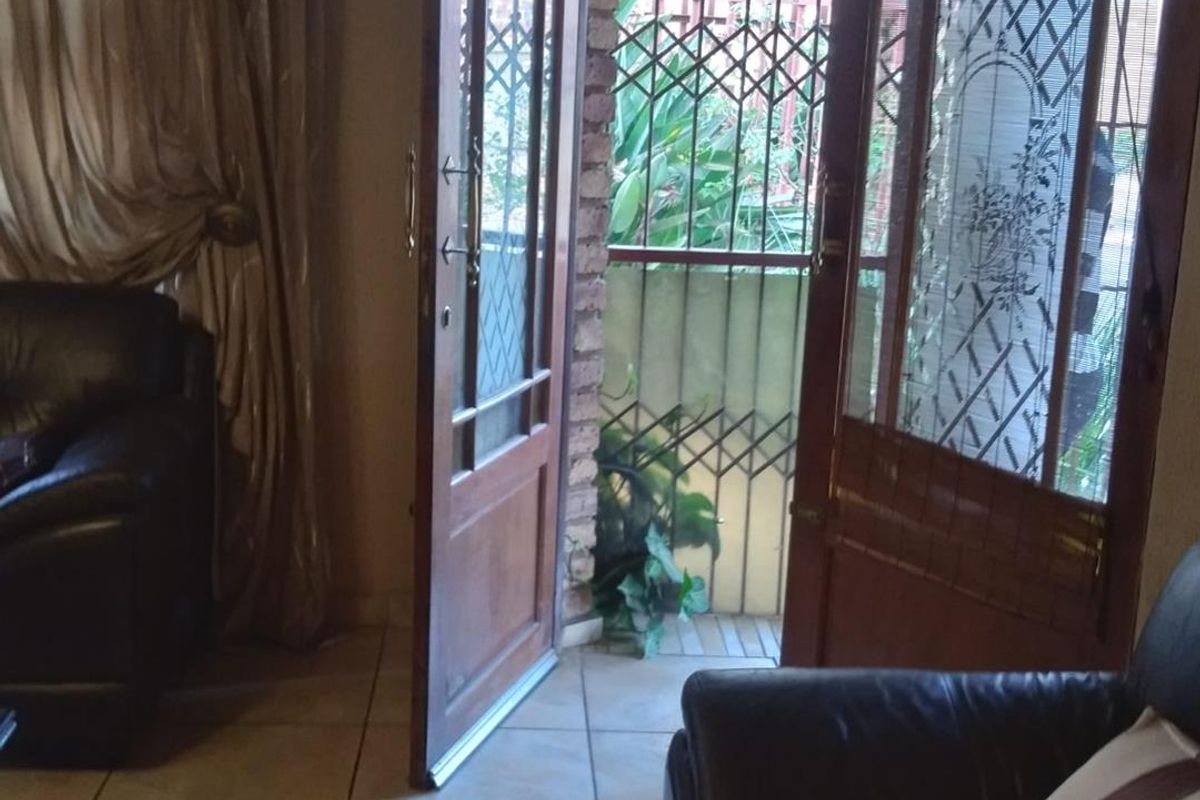 Interior living area featuring tiled flooring and double wooden doors opening to an exterior patio with security gates.