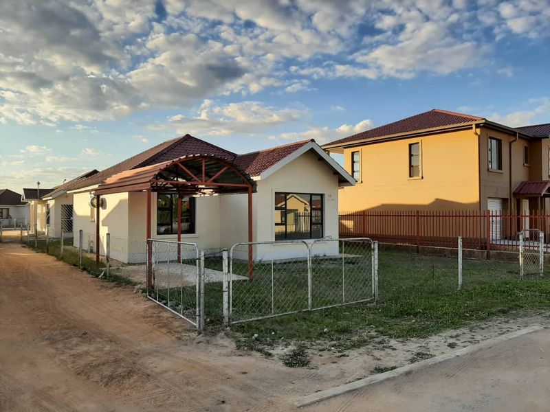 Front view of a single-story residential house featuring a tiled roof, metal carport, and chain-link perimeter fencing.