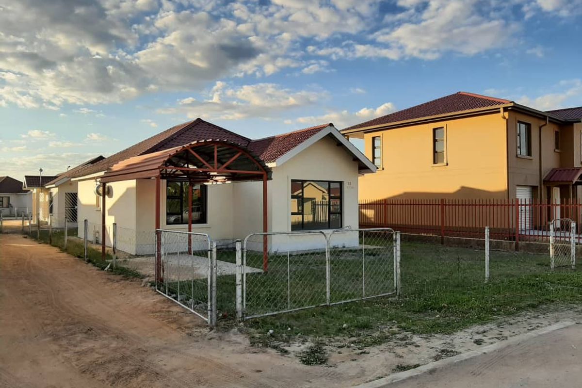 Front view of a single-story residential house featuring a tiled roof, metal carport, and chain-link perimeter fencing.