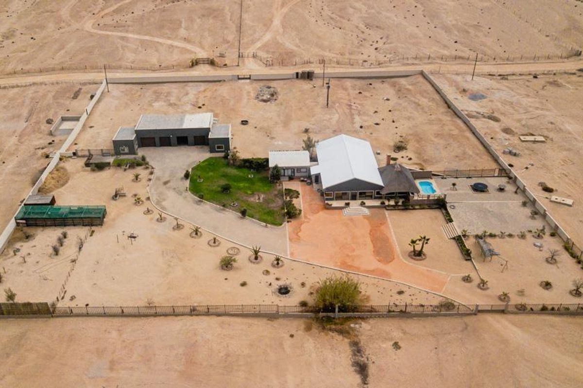 Aerial view of a small holding property featuring a main dwelling, detached garage, swimming pool, and expansive fenced grounds in a desert landscape.