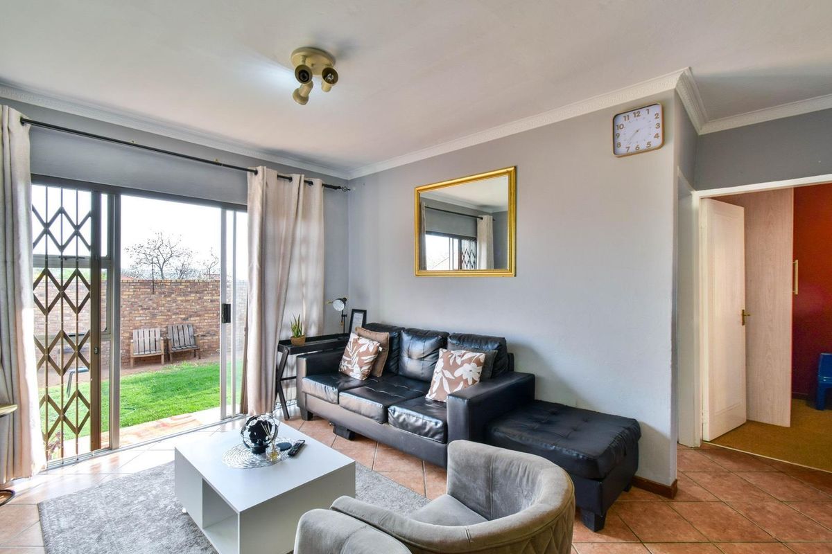 A living room featuring tiled flooring, a sliding glass door with security gate, and direct access to a private rear garden area.