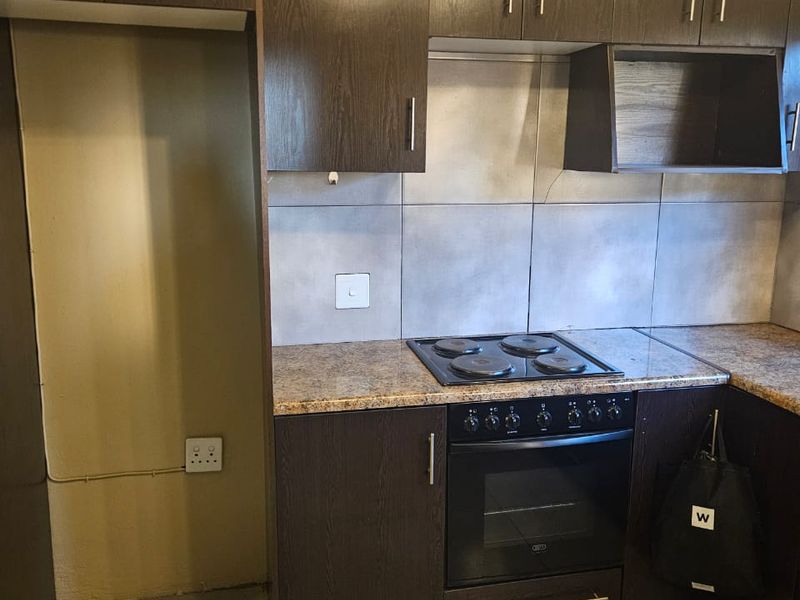 A functional kitchen featuring dark wood cabinetry, granite countertops, a built-in oven and hob, and tiled flooring with a dedicated refrigerator space.