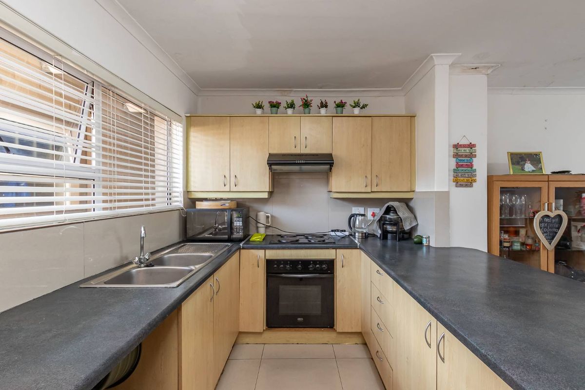 A functional kitchen featuring light wood-tone cabinetry, dark laminate countertops, a built-in oven with gas hob, and a double stainless steel sink.