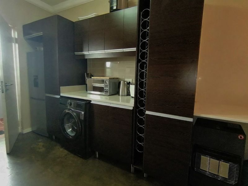 A functional laundry area featuring dark wood-finish built-in cabinetry, laminate countertops, and a tiled backsplash, providing ample storage and utility space.