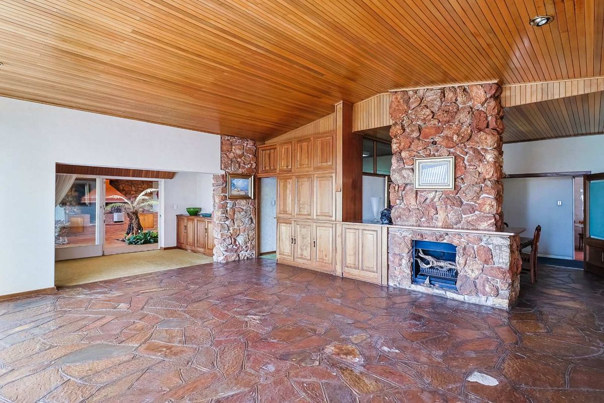 Spacious living area featuring a prominent stone fireplace, natural stone flooring, and warm timber-paneled ceilings with built-in cabinetry.