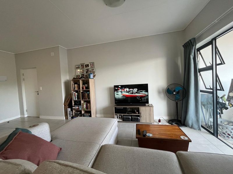 A bright living room featuring neutral tiled flooring and a large sliding glass door providing access to an outdoor area.