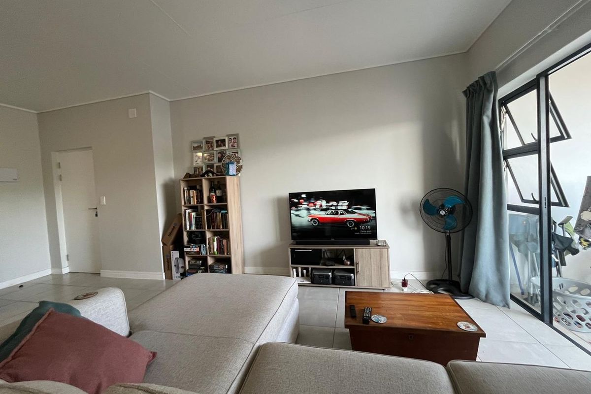 A bright living room featuring neutral tiled flooring and a large sliding glass door providing access to an outdoor area.