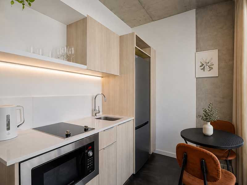 Modern compact kitchen featuring light wood cabinetry, stone countertops, integrated appliances, and an exposed concrete ceiling, creating a sleek and functional culinary space.