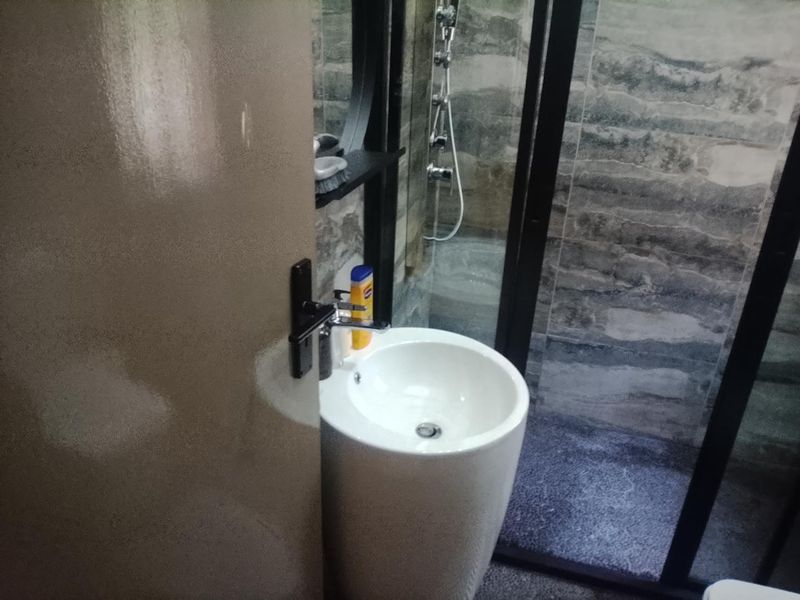 A compact bathroom featuring a modern pedestal basin with a mixer tap and a glass-enclosed shower with textured wall tiling.
