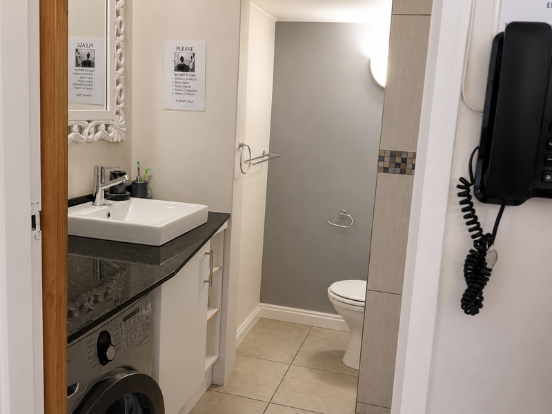 A functional bathroom featuring a vanity with granite countertop, integrated washing machine, and a separate toilet area with neutral tiling.