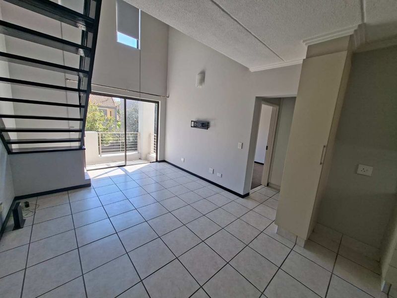 Spacious double-volume living area featuring tiled flooring, a modern metal staircase, and direct access to a private balcony.