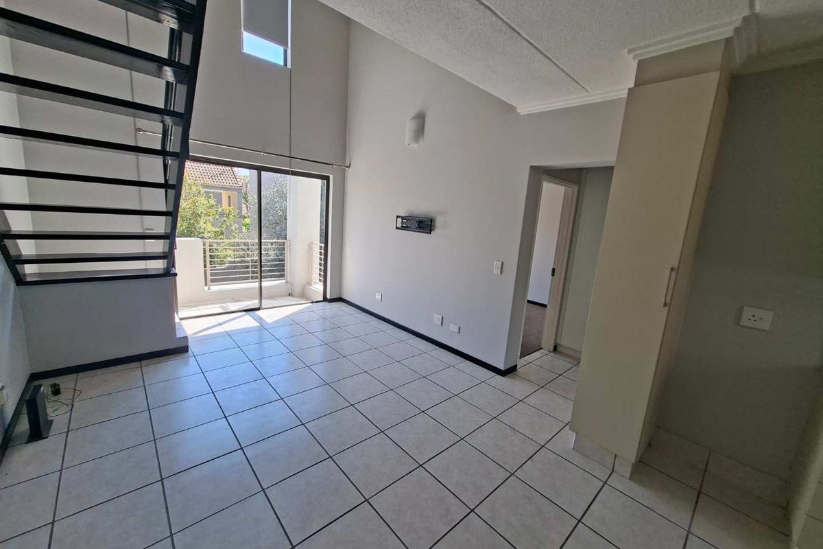 Spacious double-volume living area featuring tiled flooring, a modern metal staircase, and direct access to a private balcony.