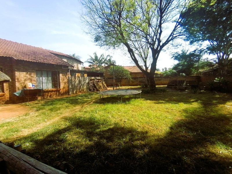 A spacious rear garden featuring a brick exterior, mature trees, and a perimeter wall, offering potential for landscaping and outdoor living.