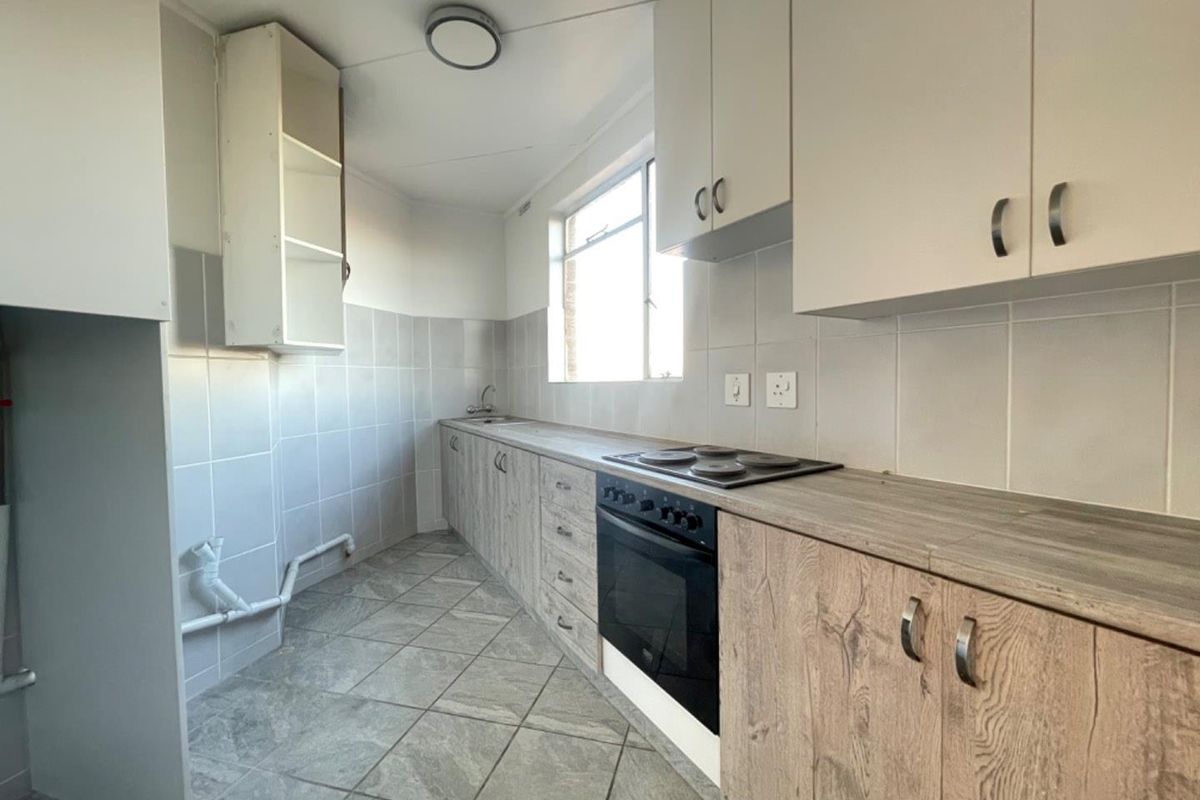 A functional kitchen featuring built-in cabinetry, laminate countertops, an integrated electric hob and oven, and tiled flooring with a neutral backsplash.