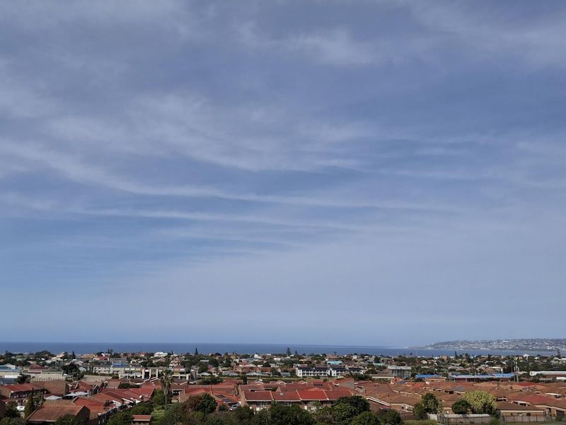 An elevated panoramic view overlooking a residential neighborhood with the coastline and ocean visible in the distance.