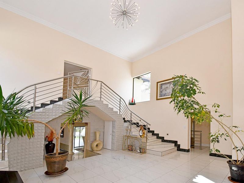 Spacious grand entrance hall featuring a prominent staircase with stainless steel balustrades, high ceilings, and polished tiled flooring.