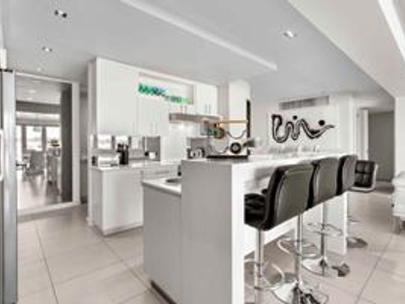Modern open-plan kitchen featuring sleek white cabinetry, a central island with breakfast bar seating, and polished tiled flooring throughout the living space.