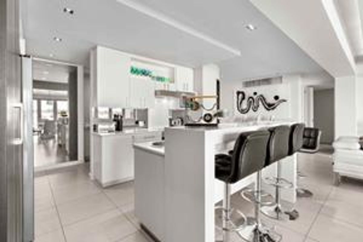 Modern open-plan kitchen featuring sleek white cabinetry, a central island with breakfast bar seating, and polished tiled flooring throughout the living space.