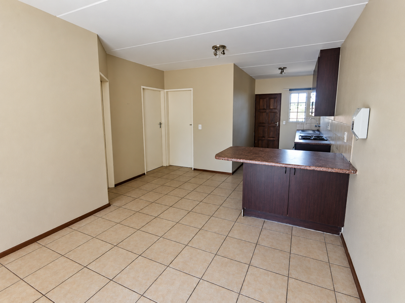An open-plan living and kitchen area featuring tiled flooring, dark wood cabinetry, and a breakfast counter, presenting a clean and functional blank canvas.