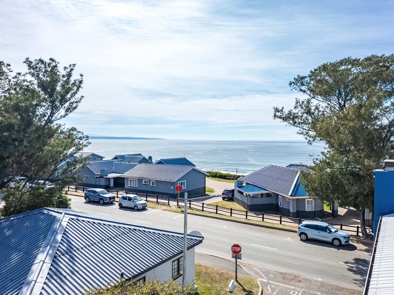 An elevated aerial view of the coastal residential street, showcasing the surrounding neighborhood layout and proximity to the ocean.