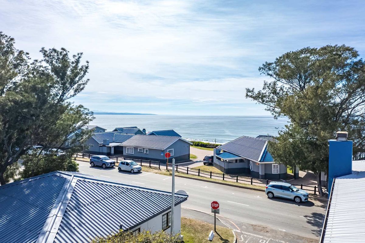 An elevated aerial view of the coastal residential street, showcasing the surrounding neighborhood layout and proximity to the ocean.