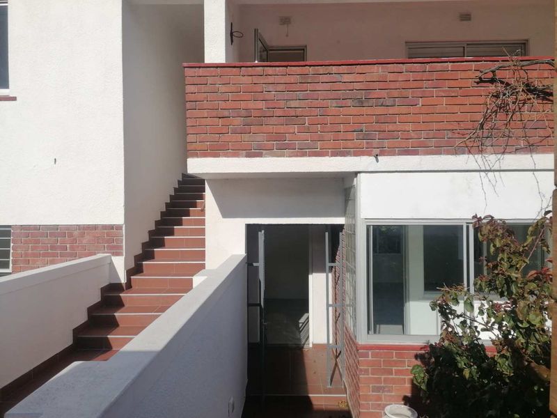 Rear exterior view of the apartment building featuring a brick balcony wall, tiled staircase, and glass block window detailing.