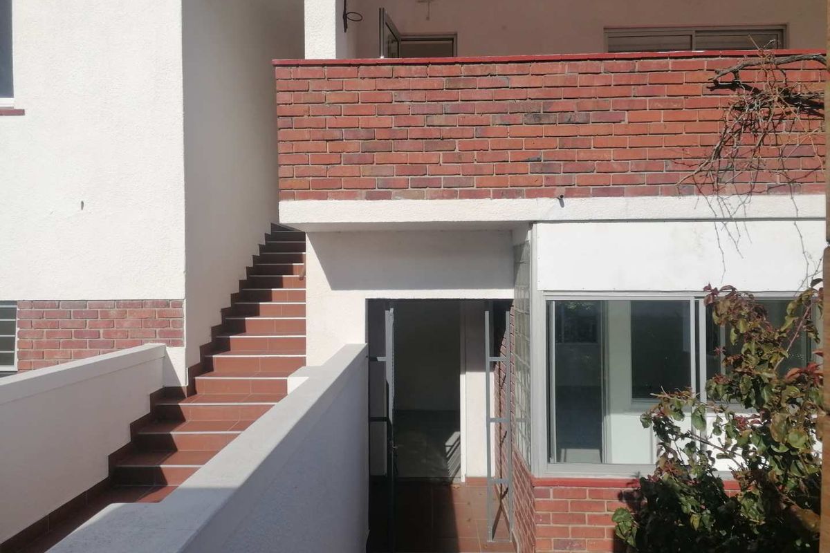 Rear exterior view of the apartment building featuring a brick balcony wall, tiled staircase, and glass block window detailing.