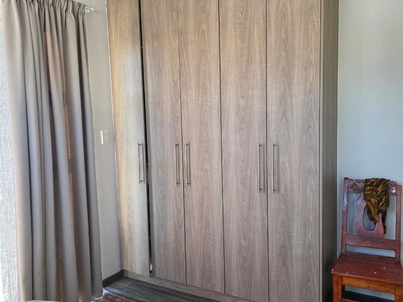 A bedroom featuring a modern, full-height built-in wardrobe with wood-grain finish and durable laminate flooring.
