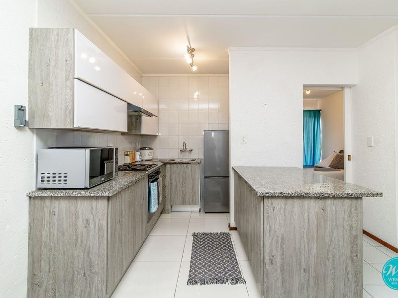 Modern kitchen featuring granite countertops, wood-grain cabinetry, gas hob, extractor fan, and tiled flooring, offering a functional and clean workspace.