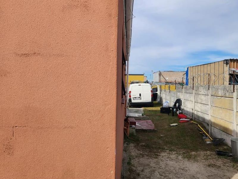 Side view of the property showing exterior wall with visible structural cracking and a precast concrete boundary wall with razor wire.