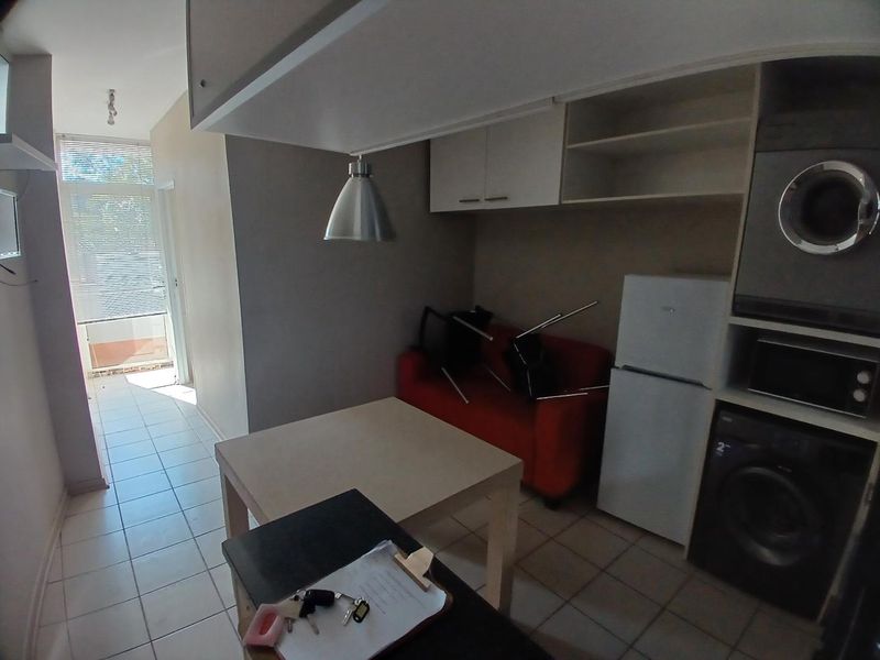 Compact open-plan living area featuring tiled floors, built-in cabinetry, and an integrated laundry space with direct access to a balcony.