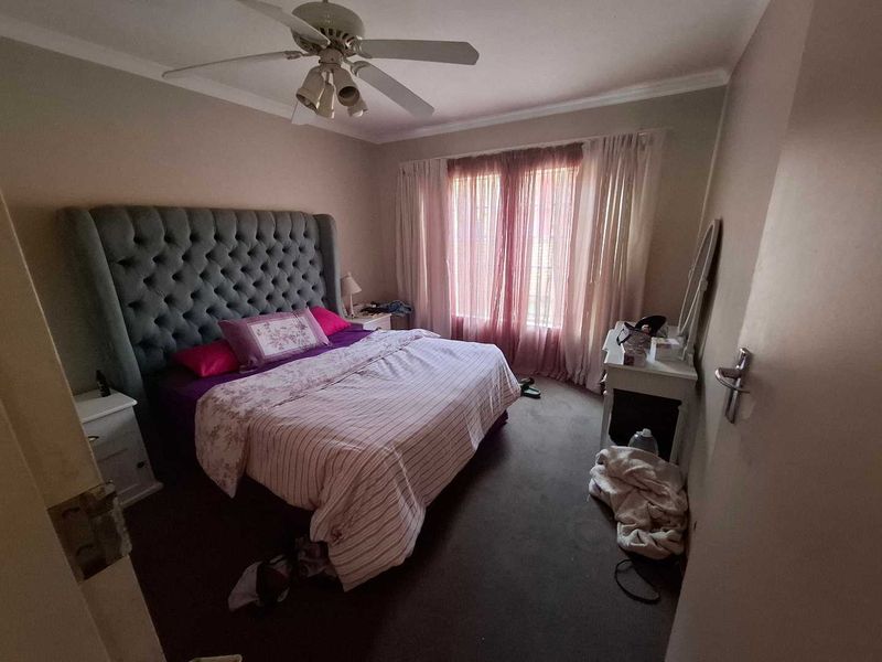 A standard bedroom featuring carpeted flooring, a ceiling fan, and large windows with curtain rails, providing a functional living space.