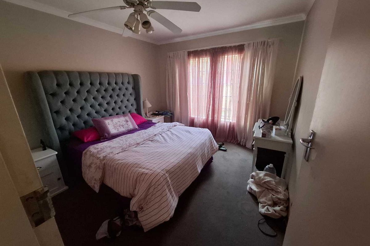 A standard bedroom featuring carpeted flooring, a ceiling fan, and large windows with curtain rails, providing a functional living space.