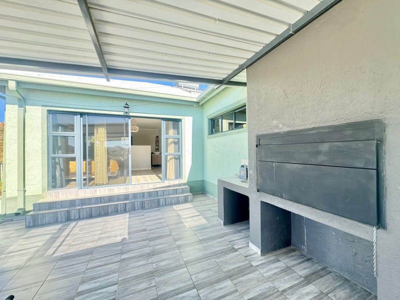 A covered patio area featuring tiled flooring, a built-in braai, and sliding glass doors providing access to the interior living space.