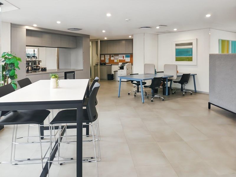 A modern open-plan office space featuring a kitchenette area, tiled flooring, and recessed lighting, suitable for collaborative work environments.