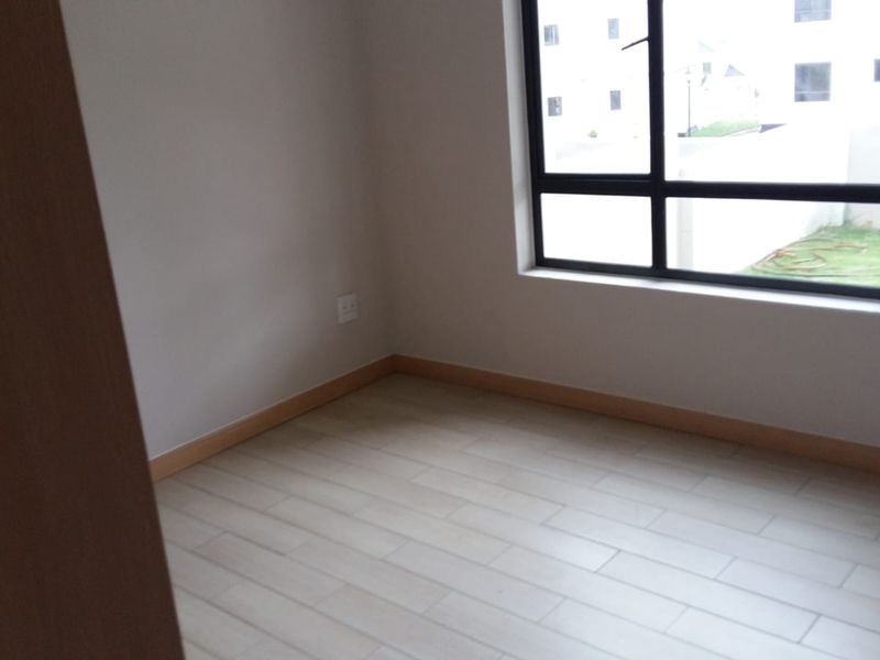 A bright, empty bedroom featuring modern tiled flooring, neutral walls, and a large aluminium-framed window providing natural light.