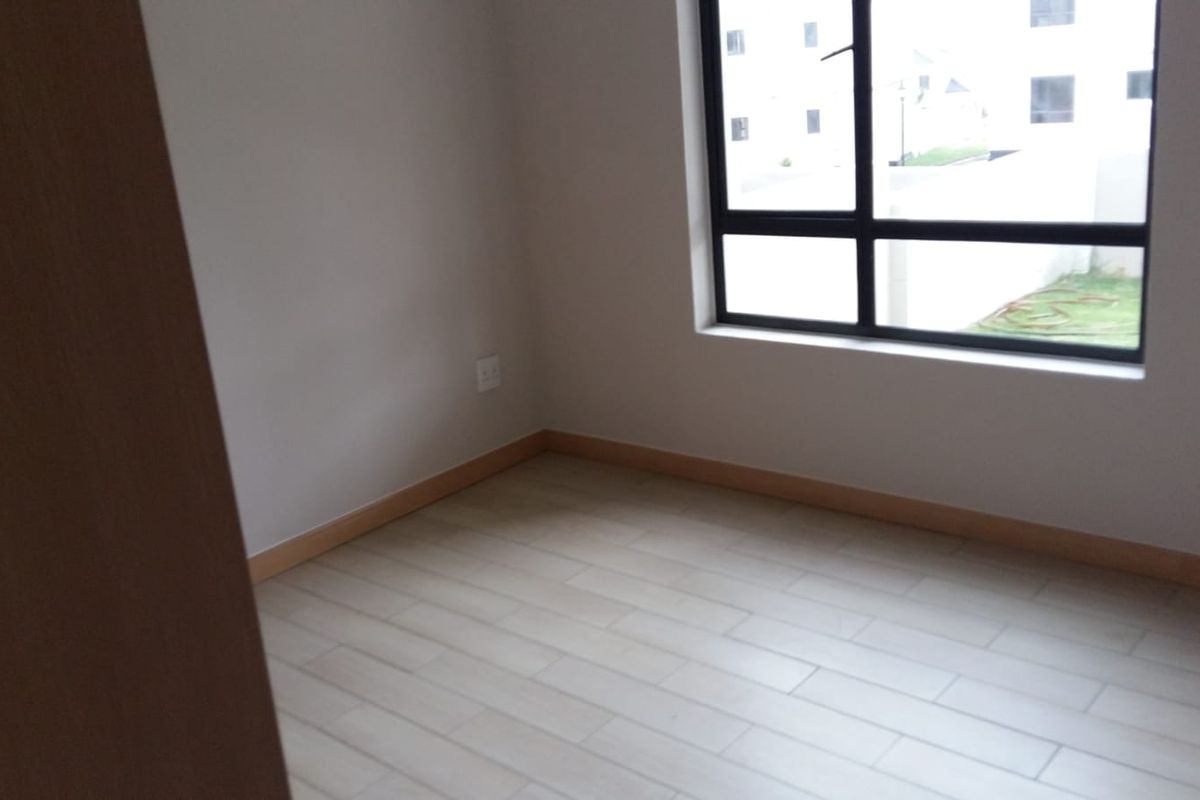 A bright, empty bedroom featuring modern tiled flooring, neutral walls, and a large aluminium-framed window providing natural light.