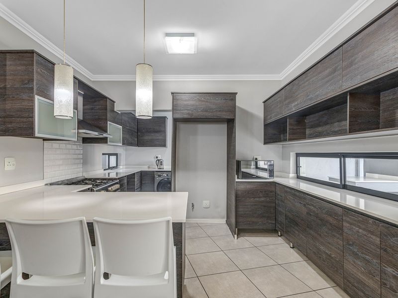 Modern kitchen featuring dark wood-grain cabinetry, stone countertops, subway tile backsplash, gas hob, and integrated storage with a breakfast bar area.