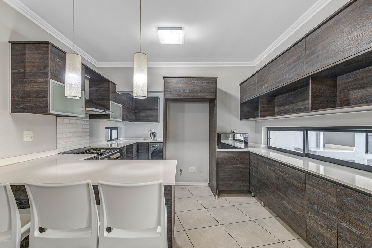 Modern kitchen featuring dark wood-grain cabinetry, stone countertops, subway tile backsplash, gas hob, and integrated storage with a breakfast bar area.