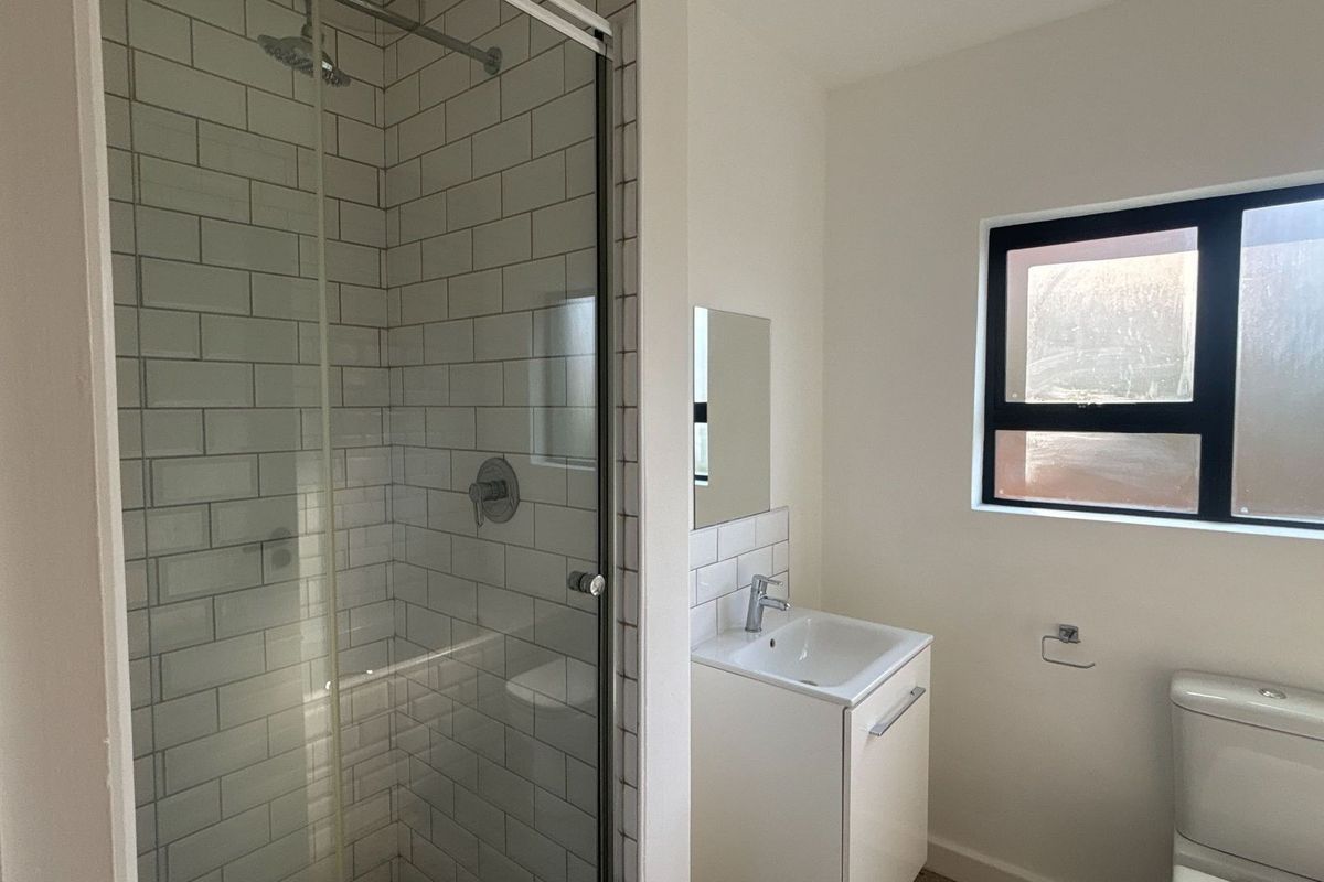 A modern bathroom featuring a glass-enclosed shower with subway tiling, a vanity basin, and a toilet.