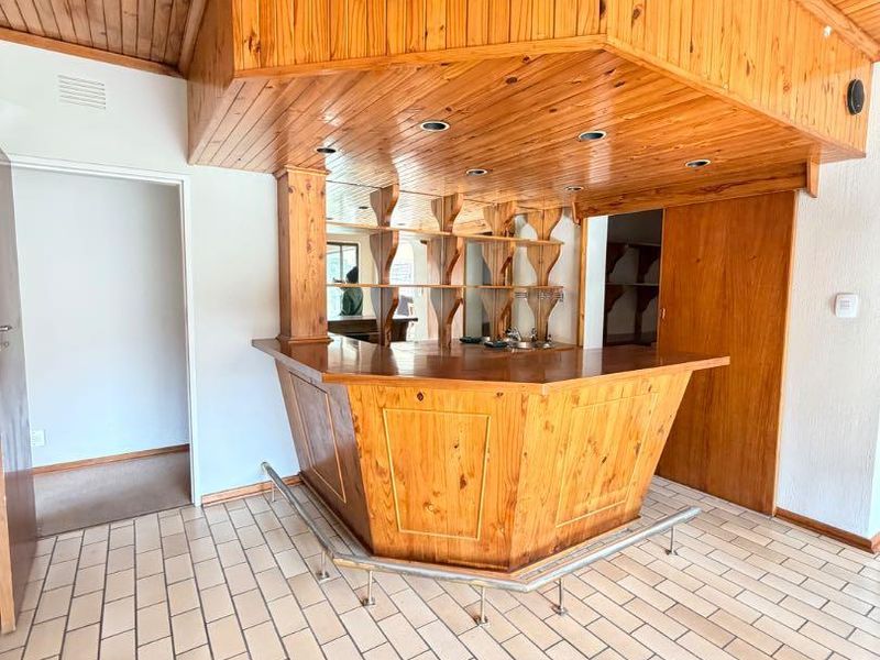 A dedicated bar area featuring built-in wooden cabinetry, a matching timber ceiling, tiled flooring, and integrated shelving, offering a classic entertainment space.