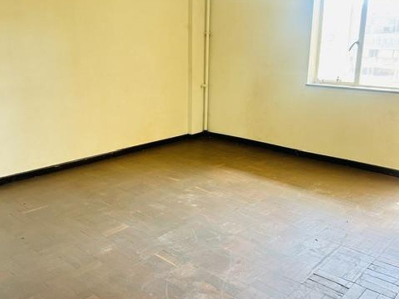 An empty bedroom featuring original parquet flooring, cornice detailing, and a window, requiring cosmetic updates to restore its appeal.