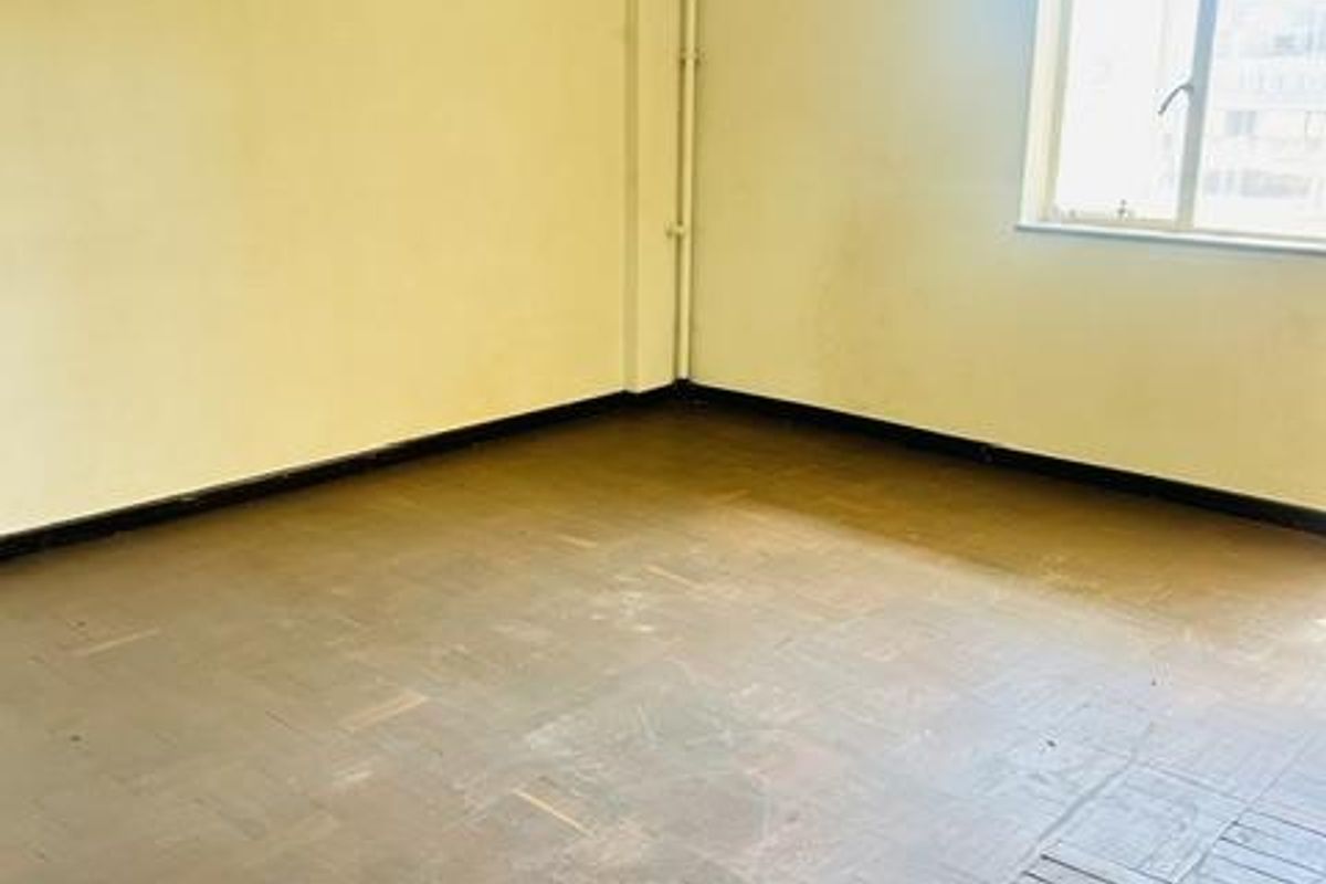 An empty bedroom featuring original parquet flooring, cornice detailing, and a window, requiring cosmetic updates to restore its appeal.