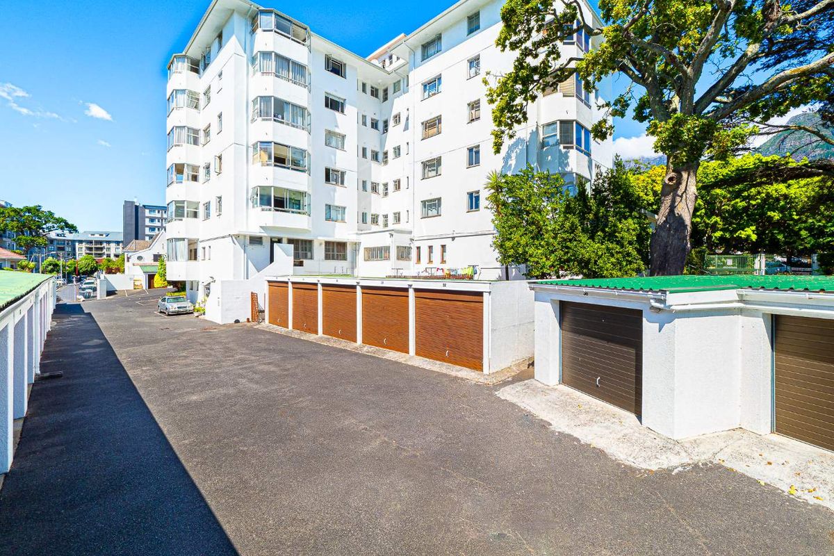 Exterior view of a multi-story apartment building featuring a row of individual lock-up garages and paved driveway access.