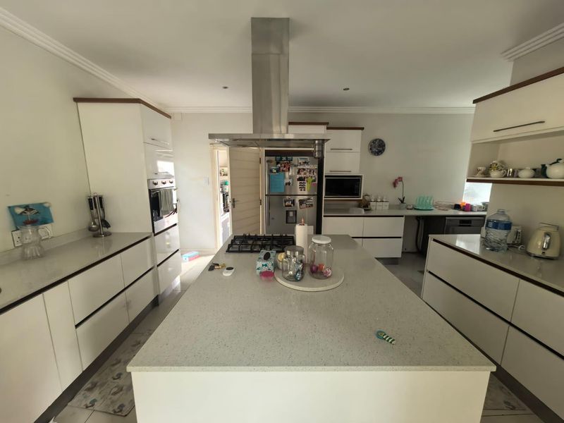 Modern kitchen featuring a central island with a gas hob, stainless steel extractor fan, built-in appliances, and ample white cabinetry with quartz countertops.