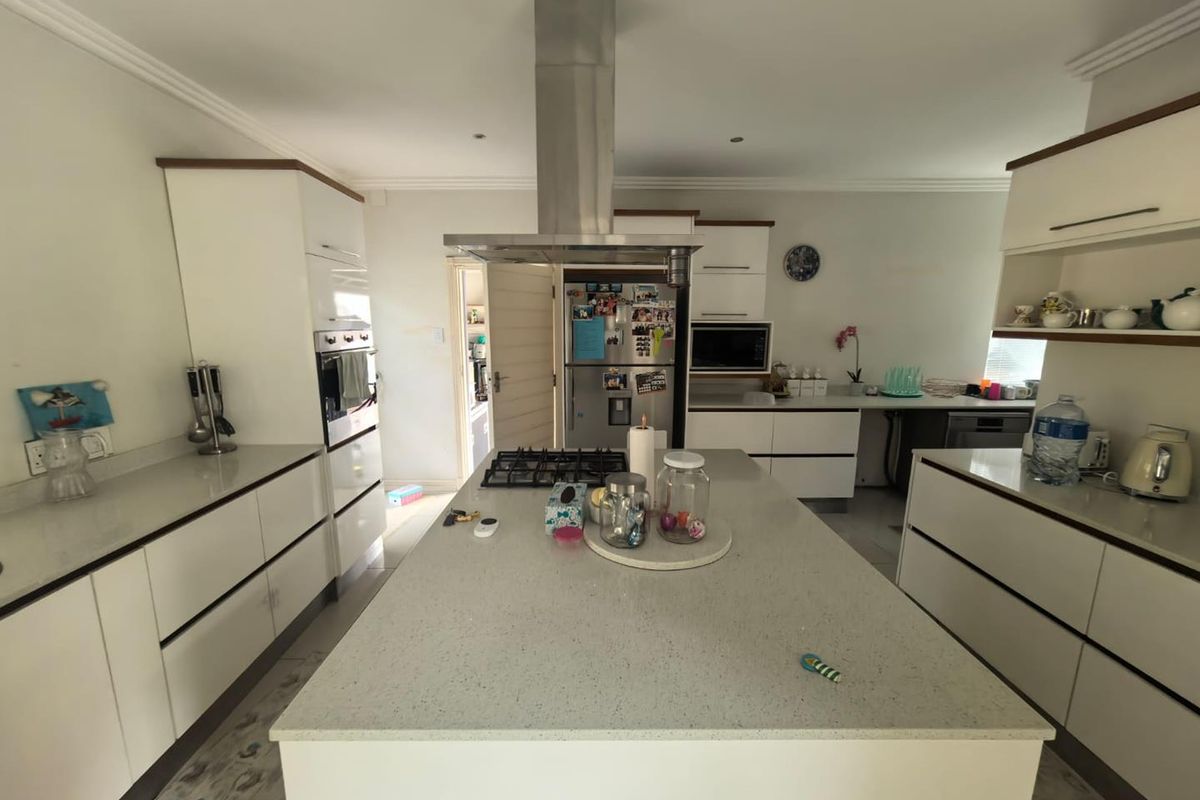 Modern kitchen featuring a central island with a gas hob, stainless steel extractor fan, built-in appliances, and ample white cabinetry with quartz countertops.