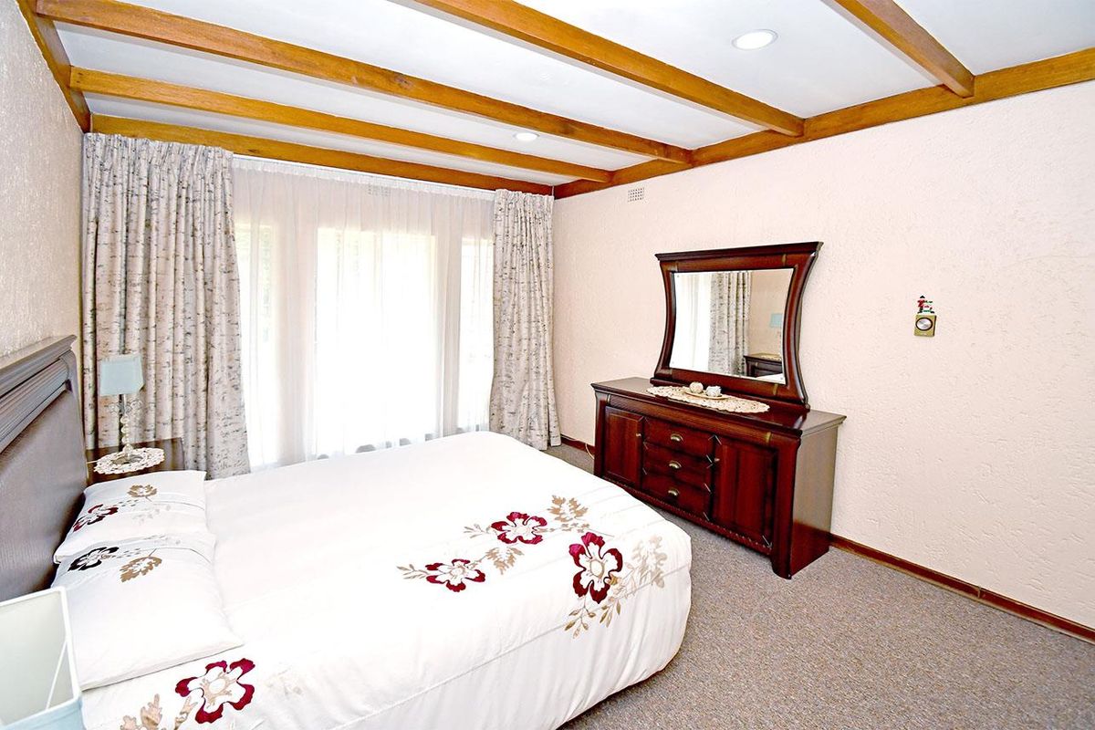 A bedroom featuring exposed timber ceiling beams, carpeted flooring, and large windows with curtains, providing a classic and functional living space.