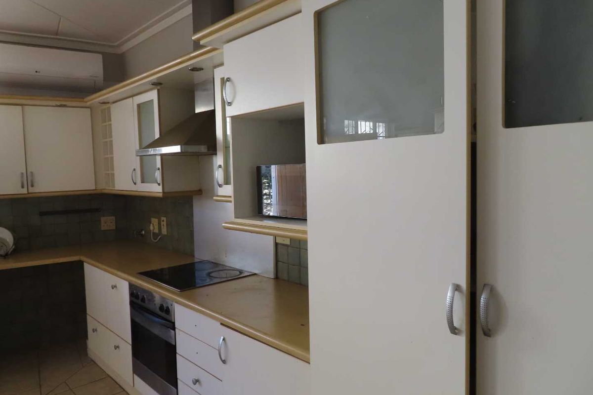 A functional kitchen featuring white cabinetry, integrated oven, electric hob, stainless steel extractor fan, and tiled flooring.